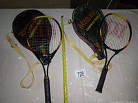 Two Wilson Sampras Tour 25 tennis rackets with their corresponding protective cases laid flat with a tape measure for scale.