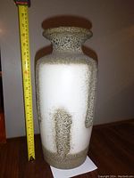 Front view of beige and brown speckled ceramic vase next to measuring tape showing height about 17 inches.