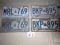 Four Ontario vehicle license plates from 1973, two pairs with numbers MRL 769 and BKP 895, some showing rust and dirt