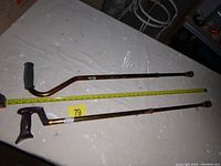 Two adjustable metal walking canes laid flat with measuring tape alongside. One cane has a rubber curved handle and the other an angular black plastic handle. Both have rubber tips and adjustable height sections.