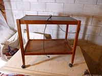 Full view of the wooden warming tray cart on wheels showing the lower shelf and black warming tray top with electrical cord.