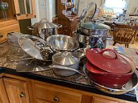 Photo showing the range of stainless steel saucepans, stock pots, colander, grater, and the red enameled cast iron Dutch oven.