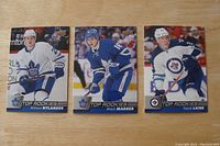 Photo showing three NHL rookie cards with players William Nylander, Mitch Marner, and Patrik Laine in their team jerseys on a wooden surface.