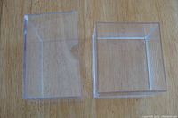 Clear plastic card holder box shown disassembled into two parts: bottom container and top lid with a thumb cutout.