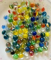 Top-down photo showing a colorful assortment of glass marbles with swirled internal patterns on a floral background.