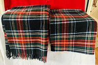 Two plaid throw blankets with fringed edges displayed side by side over a white surface with red background.