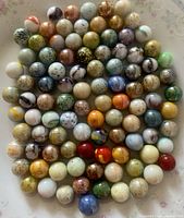 Overhead photo of approximately 100 vintage art glass marbles with varied speckled and confetti patterns in multiple colors, arranged closely on a white background.