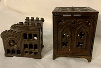 Two vintage cast iron coin banks, a building and a safe, shown together from the front and side, highlighting shape and detail.