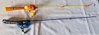 Two children's fishing rods laying flat, one Diego-themed orange and yellow rod, and one blue and black Shakespeare rod.