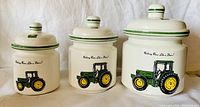 Set of three ceramic John Deere canisters with lids showing front and side views, displayed in a row.