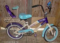 Profile and front angle view of Journey Girls bicycle showing doll seat, bell, teal and purple color scheme, and 13-inch tires.