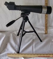 Front-side view of the black telescope mounted on a collapsible tripod. Shows angled eyepiece and focusing handle.