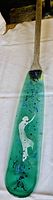 Full view of the green glass paddle blade with the white dancing woman design and wooden handle attached.
