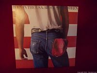 Front cover of Bruce Springsteen Born in the USA vinyl record album showing jeans and red cap with red and white stripes background.