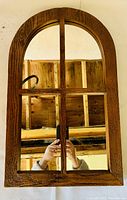 Dome mirror with 4 separate rectangular panes divided by wood, dark stained pine wood frame, arched top dome shape, reflective mirror surface showing hand holding a phone to take the photo.