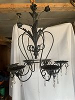 Front view of black metal chandelier with rose bud top and six scalloped candle holders with hanging crystal pendants