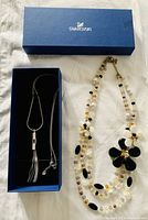 Swarovski blue box with silver chain necklace inside and a floral crystal beaded necklace outside the box.