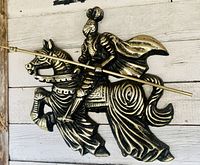 Close-up photo of metal wall hanging showing knight in full armor on armored horse holding lance - front view