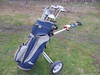 Full view of blue and gray Dantrek golf bag mounted on three wheeled push cart outdoors on grass turf.