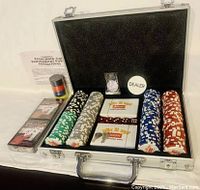 Open aluminum case showing poker chips, playing cards, dice, dealer button, and accessories.