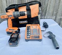 Full lot displayed on table in front of wooden background includes cordless drill, charger, batteries, handle, and carrying bag.