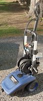 Blue Simoniz electric pressure washer 1800 PSI standing on gravel outdoors with hose reel and handle visible.