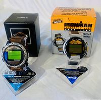 Two Timex men's watches displayed on stands in front of their boxes: Timex Expedition Digital Compass and Timex Ironman Triathlon.
