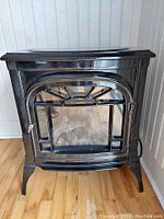 Front view of black free standing electric heater with glass door and metal frame showing decorative window detail.