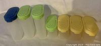 Front view of seven Tupperware Modular Mate spice containers arranged in a row showing various lid colors and sizes.