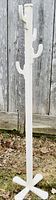 Photo of white painted wooden coat hanger rack standing against a wooden fence taken outdoors, showing front and side views.