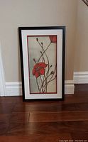 Front view of framed artwork depicting a red flower with stems and buds in a black frame with red matte.