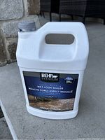 Photo of a white 1-gallon container with a gray cap showing the Behr Premium wet-look sealer label for concrete and paver protection.