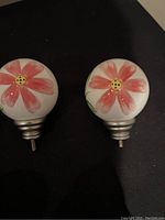 Pair of ceramic curtain rod finials with pink flower design, metallic screw base visible