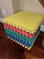 Stack of interlocking foam floor tiles in yellow, red, green, and blue colors, neatly stacked showing edge interlocking design.