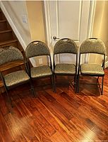 Four upholstered folding chairs with metal frames arranged in a row on hardwood floor.