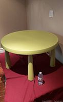 Full view of round green table with solid green finish and thick legs on a red mat placed on wood floor.