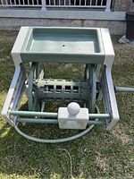 Side view showing the hose reel box with winding handle and attached hose on grass background.