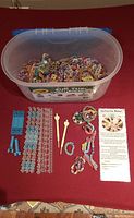Container with colorful rubber bands and kit contents including plastic weaving boards, hooks, rubber band bracelets, and instruction manual laid out.