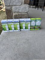 Six Philips Energy Saver individual bulb packages and two EnerSaver bulb packages arranged on outdoor concrete floor.