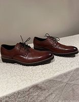 Side view of men's brown leather dress shoes on a patterned surface showing the full profile and rubber outsole with tread