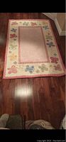 Full view of the Pottery Barn Olivia carpet laid on wooden flooring showing butterfly border pattern and solid center field.
