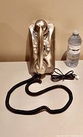 Front view of metallic vintage style Pottery Barn phone with coiled cord and handset, sitting next to water bottle for scale.