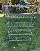 Front view of the metal wine rack standing outdoors on grass, showing all five shelves designed for wine bottle storage with light surface rust.