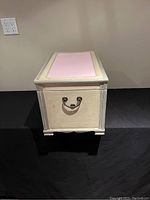 Side view of the wooden chest showing textured cream paint, raised yellow trim, and central pink panel on top.