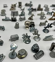 Multiple metal Monopoly game tokens arranged on white background, showing a variety of shapes and finishes including brass and pewter pieces from different Monopoly editions.