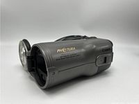 Side view showing lens details, Canon Photura 135 name, zoom range 38-135mm, and aperture f/3.2-2.8. Silver grey finish with wrist strap attached.