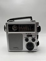 Front view of silver Eton FR-250 radio showing speaker, tuning dial, flashlight, hand crank, and carry handle.