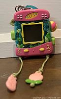 Front view of the Littlest Pet Shop Tamagotchi Turtle virtual pet showing screen, buttons, and pull-string legs with charms.