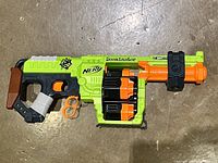 Top-down photo of green and orange Nerf Zombie Strike Doominator blaster showing large round black dart drum side and ergonomic grip