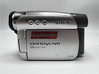 Side view of silver Sony Handycam DCR-HC26 with labels indicating Carl Zeiss Lens, Touch Panel LCD, and 20x Optical Zoom.